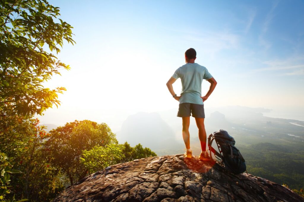Man standing on a mountaintop at sunrise looking out over a valley, symbolizing hope and a new beginning in recovery.