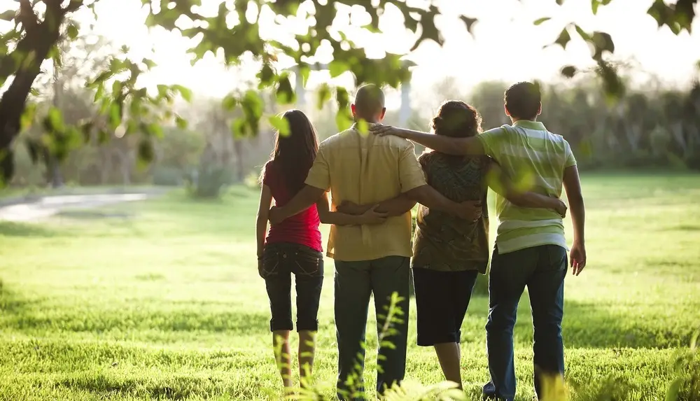 Family walking arm-in-arm through a sunlit green park, supporting each other in recovery.